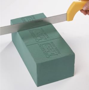 Corte de um tijolo de espuma floral verde OASIS com uma faca de cabo amarelo.